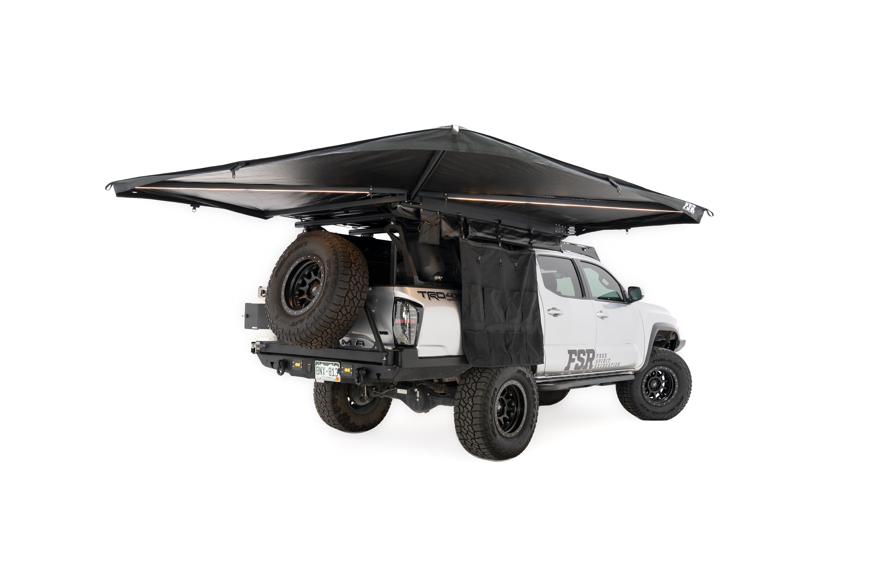Photo of deployed 270 V2 Awning by Freespirit Recreation with integrated lighting displayed on a Toyota Tacoma pickup in white cyc with the gear grid option shown.