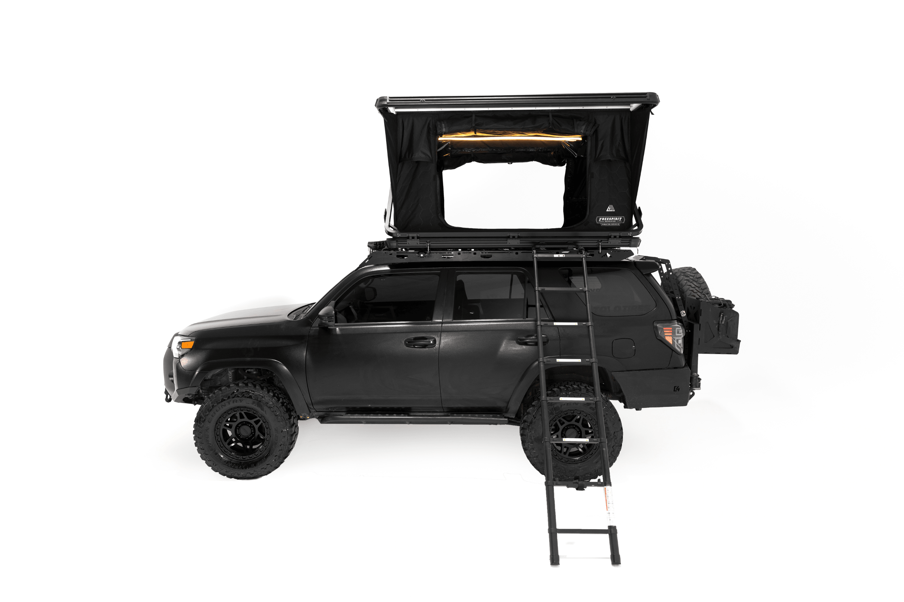 Exterior photo of a deployed Evolution V2 Standard - Rooftop Tent by Freespirit Recreation displayed in a white cyc photo cyclorama on top of a black Toyota 4Runner with ladder deployed and dimmable LED light turned on.
