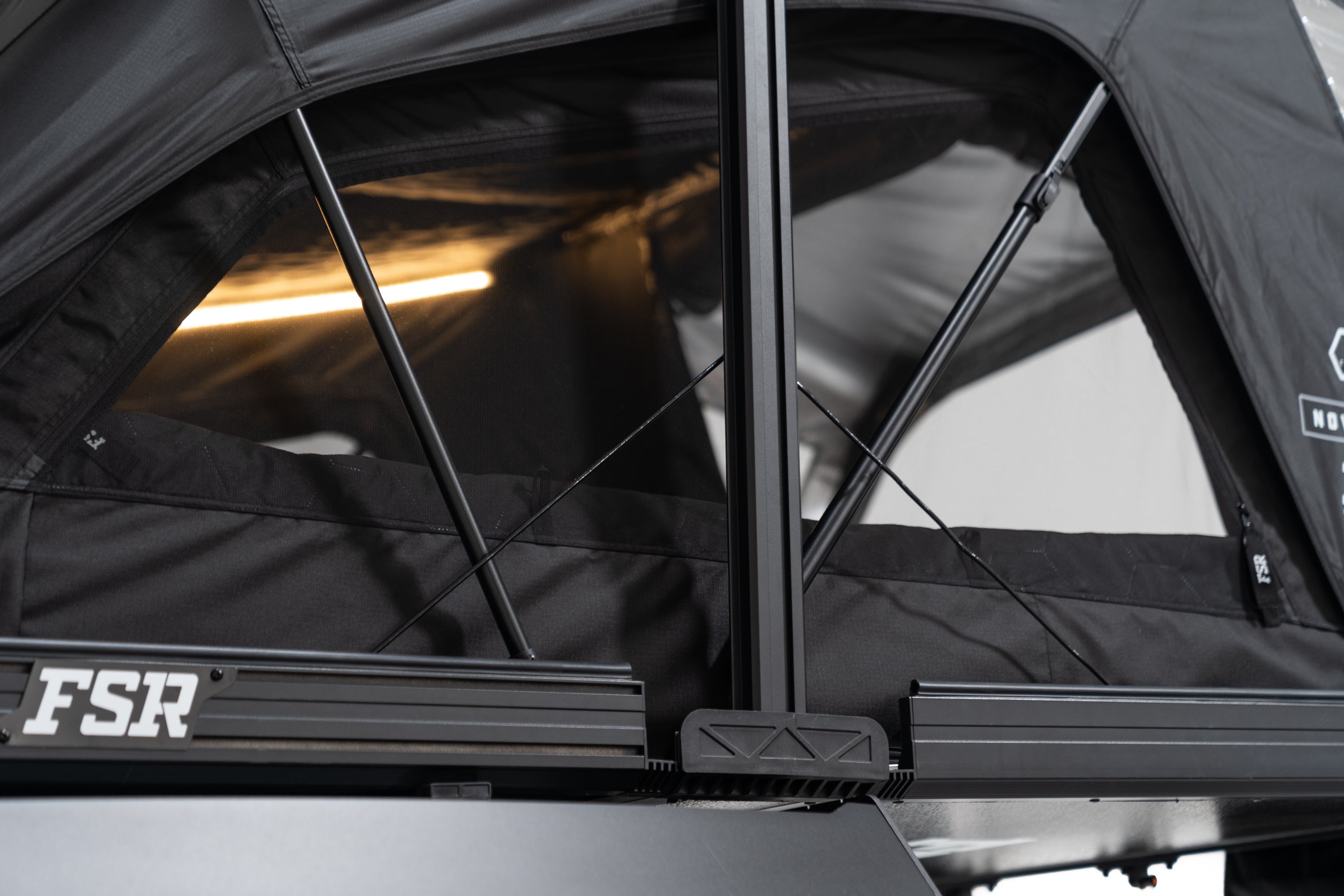 Exterior Close up photo of the Nova King rooftop tent cable support system with the tent windows open and lights on.