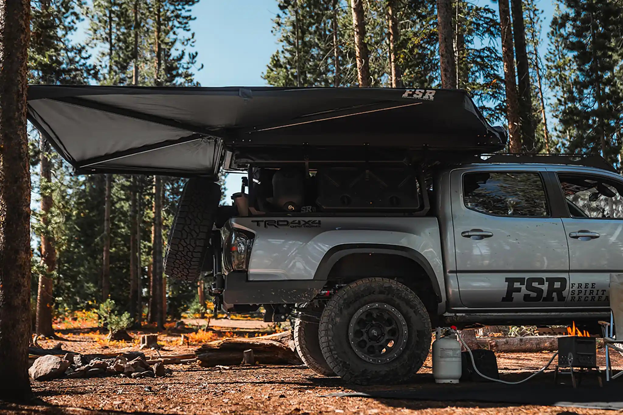 Free Spirit Recreation 270 Awning installed on a Toyota Tacoma deployed while camping in a forested setting