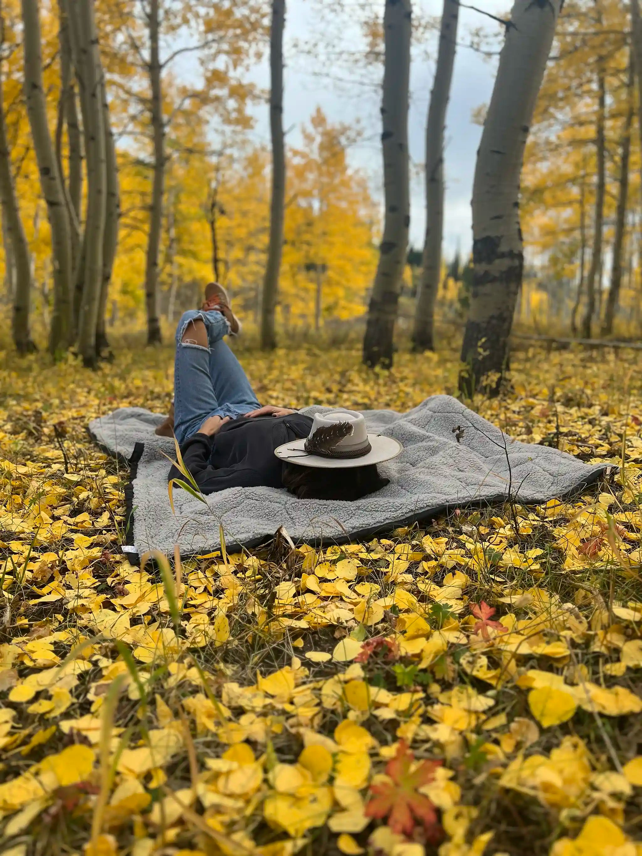 Person resting on the FSR Anywhere Poncho Camping Blanket in a forest surrounded with yellow autumn leaves