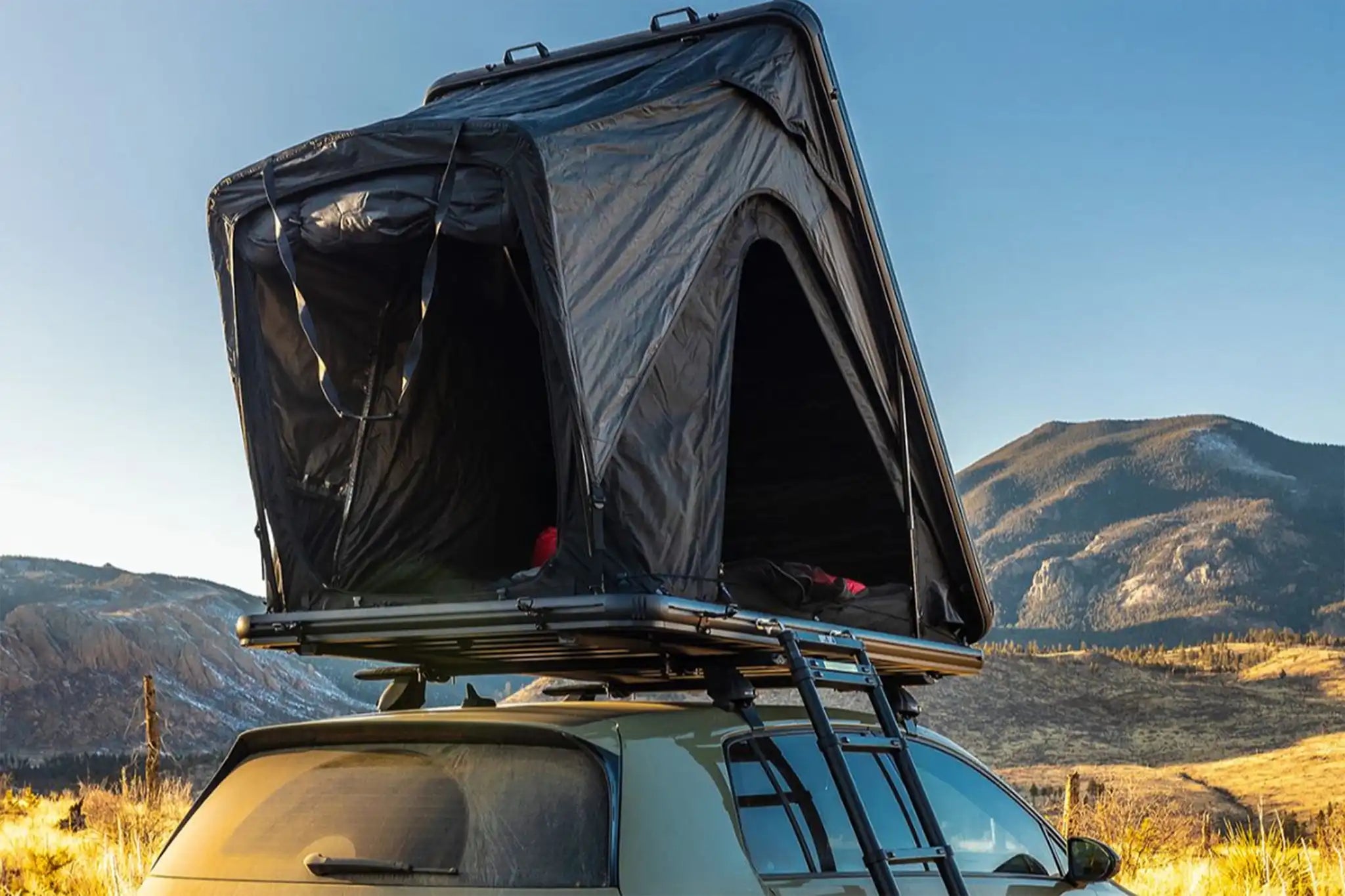 Photo of a person camping in an FSR Aspen Lite Standard Rooftop Tent by Free Spirit Recreation with windows and doors open infront of a mountain range at sunrise
