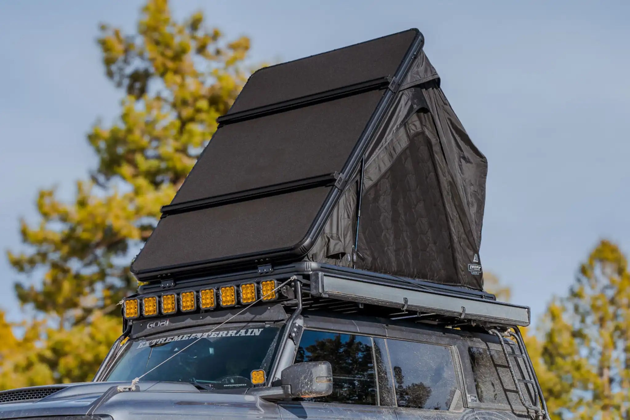 Exterior photo of the FSR Aspen Lite XL Rooftop Tent open and installed on a Ford Bronco while camping in a forested setting