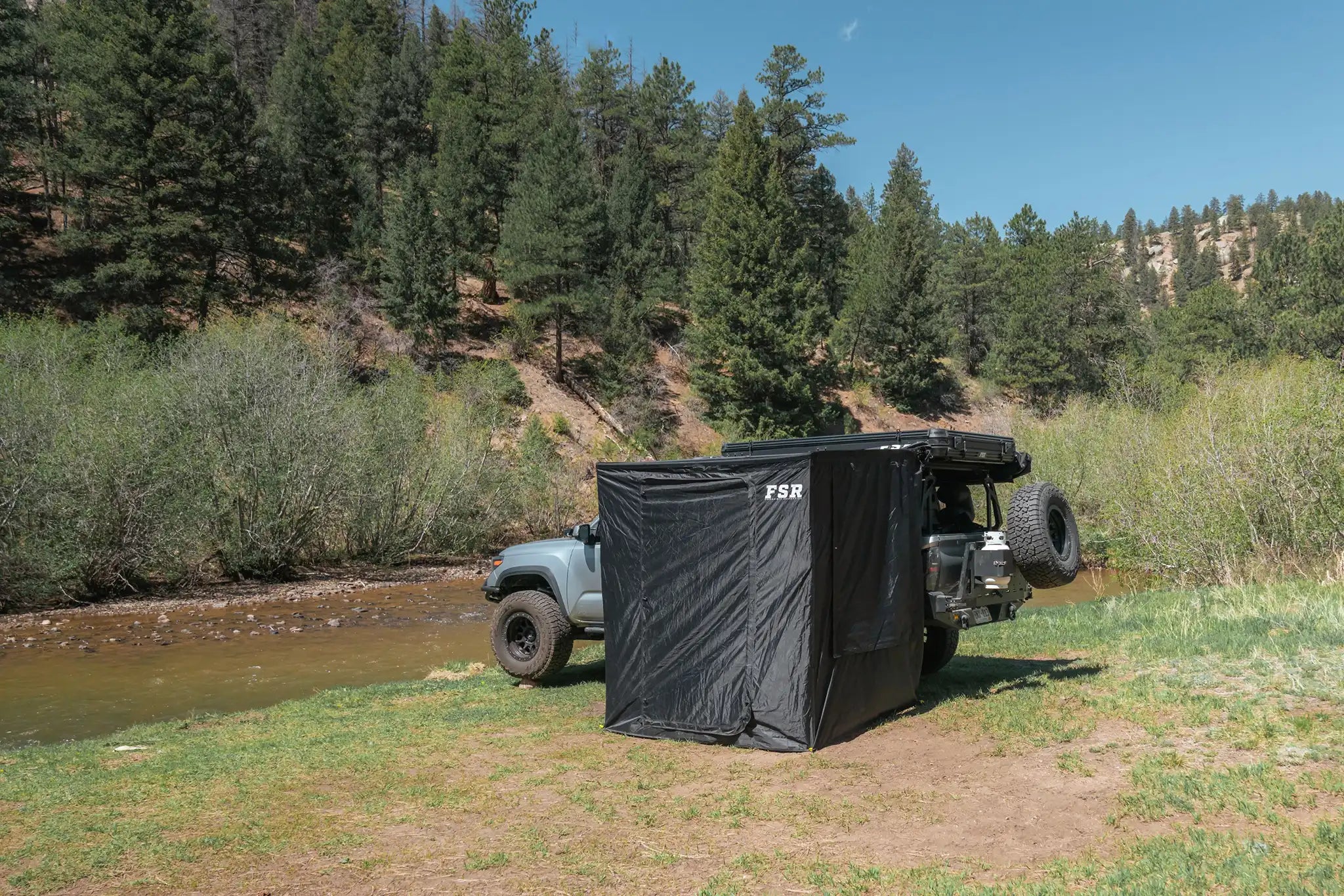 Landscape view of the FSR Double Shower Awning & Privacy Tent installed on a Freespirit Recreation Roof Top Tent while camping in a Tacoma overland truck build with a river visible in the background