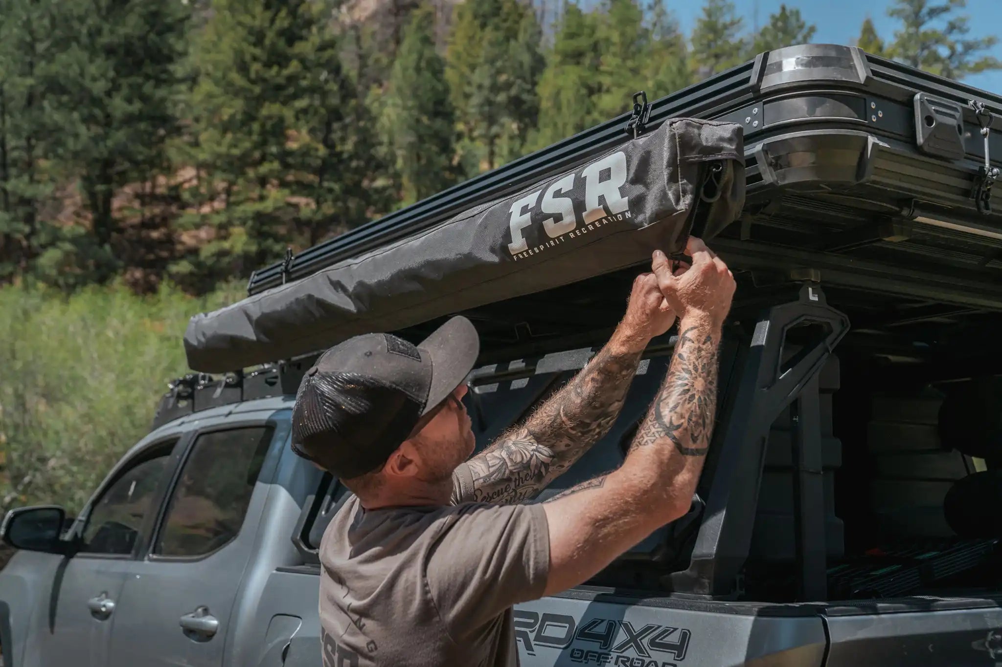 Person closing up the FSR Double Shower Awning & Privacy Tent and securing it in the included storage bag mounted to a Freespirit Recreation Rooftop Tent