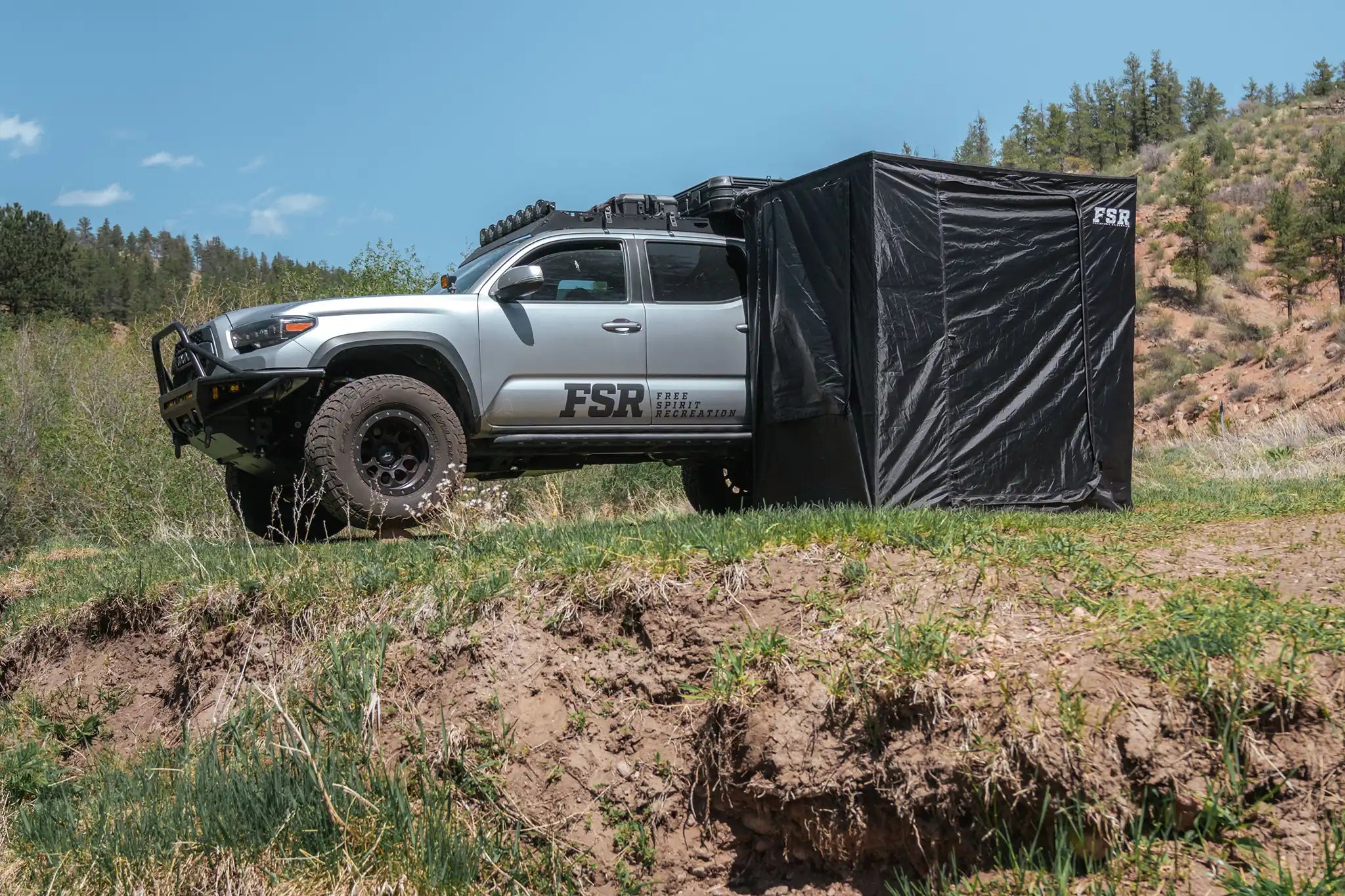 Image of the FSR Double Shower Awning & Privacy Tent installed on a Toyota Tacoma overland truck while campingwith forested hills in the background