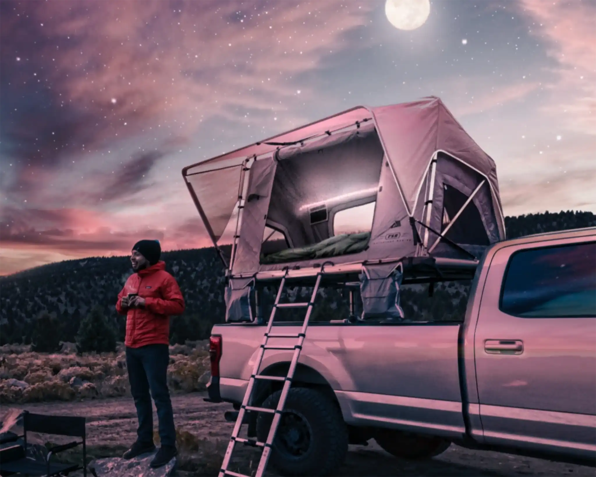Man standing next to an early Adventure Series FSR Rooftop Tent with gas struts mounted on a truck bed rack and setup for camping under a stary night sky in 2017