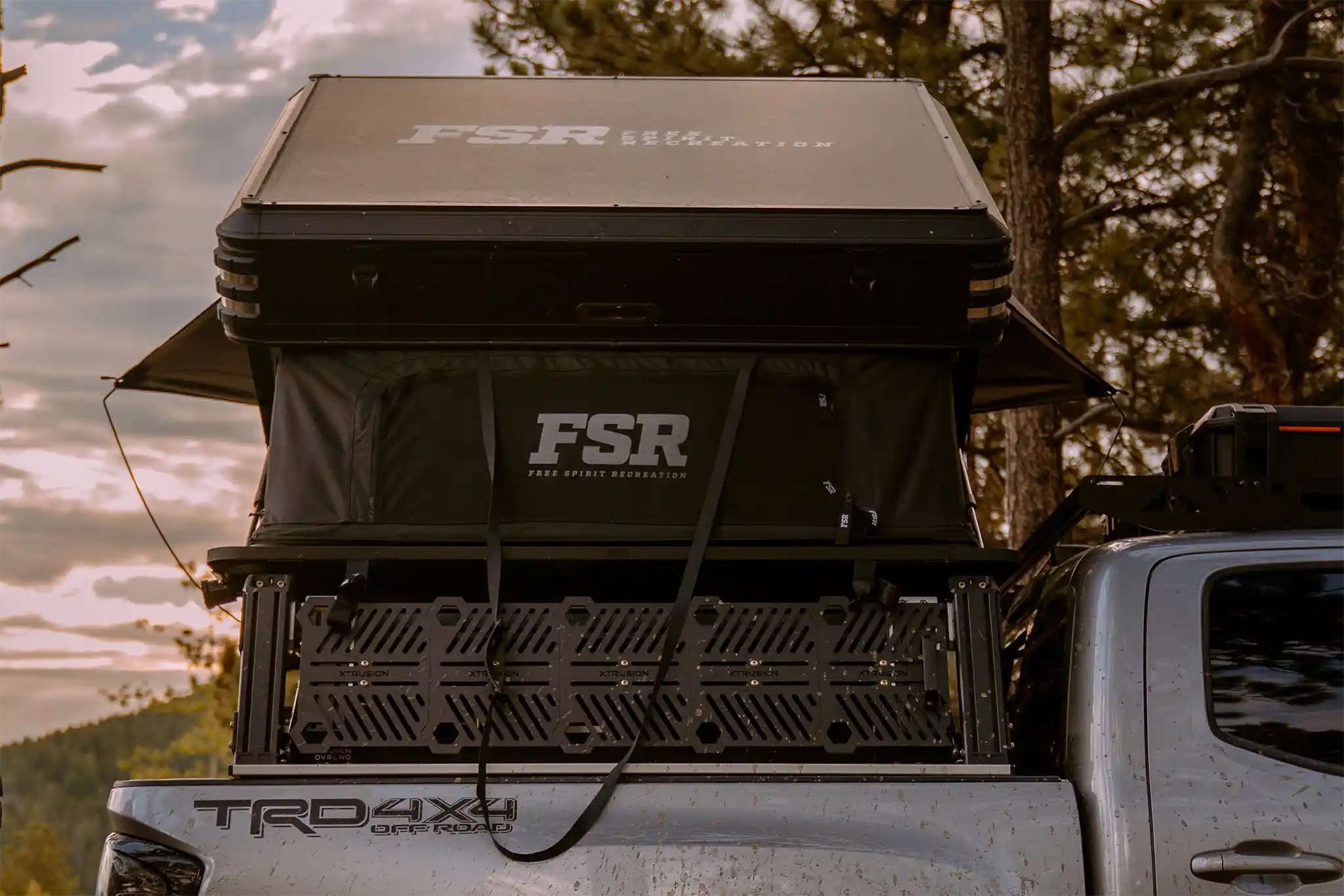Rear-facing image of the FSR rooftop tent installed on a truck bed rack with a scenic wooded sunset view in the background
