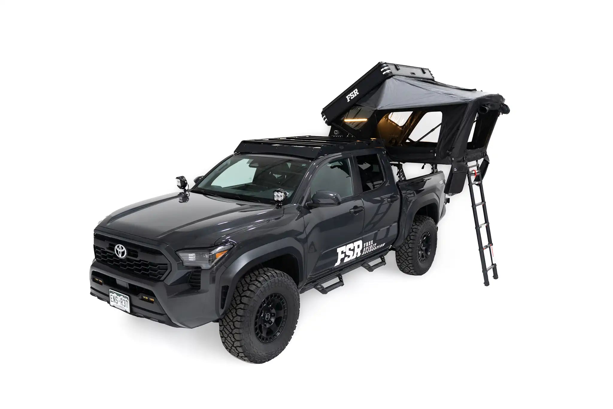 Front angle exterior photo of FSR Kali hardshell rooftop tent - mounted on the truck bed rack of a 4th gen Toyota Tacoma with lights on and windows open.