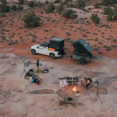 Desert camping scene with a truck and overland trailer equipped with a variety of products from Freespirit Recreation - including roof top tents, awnings, and other overlanding gear - with a campfire visible in the foreground