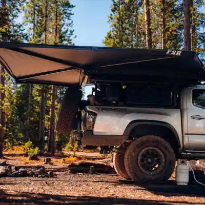 Toyota truck with an FSR 270 Awning installed and deployed in a forest setting while camping