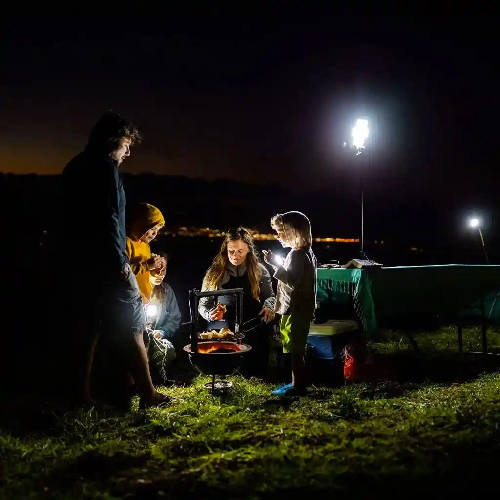 Family gathered around a campfire at night with FSR ReadyLight LED camping lights providing light to the campsite.