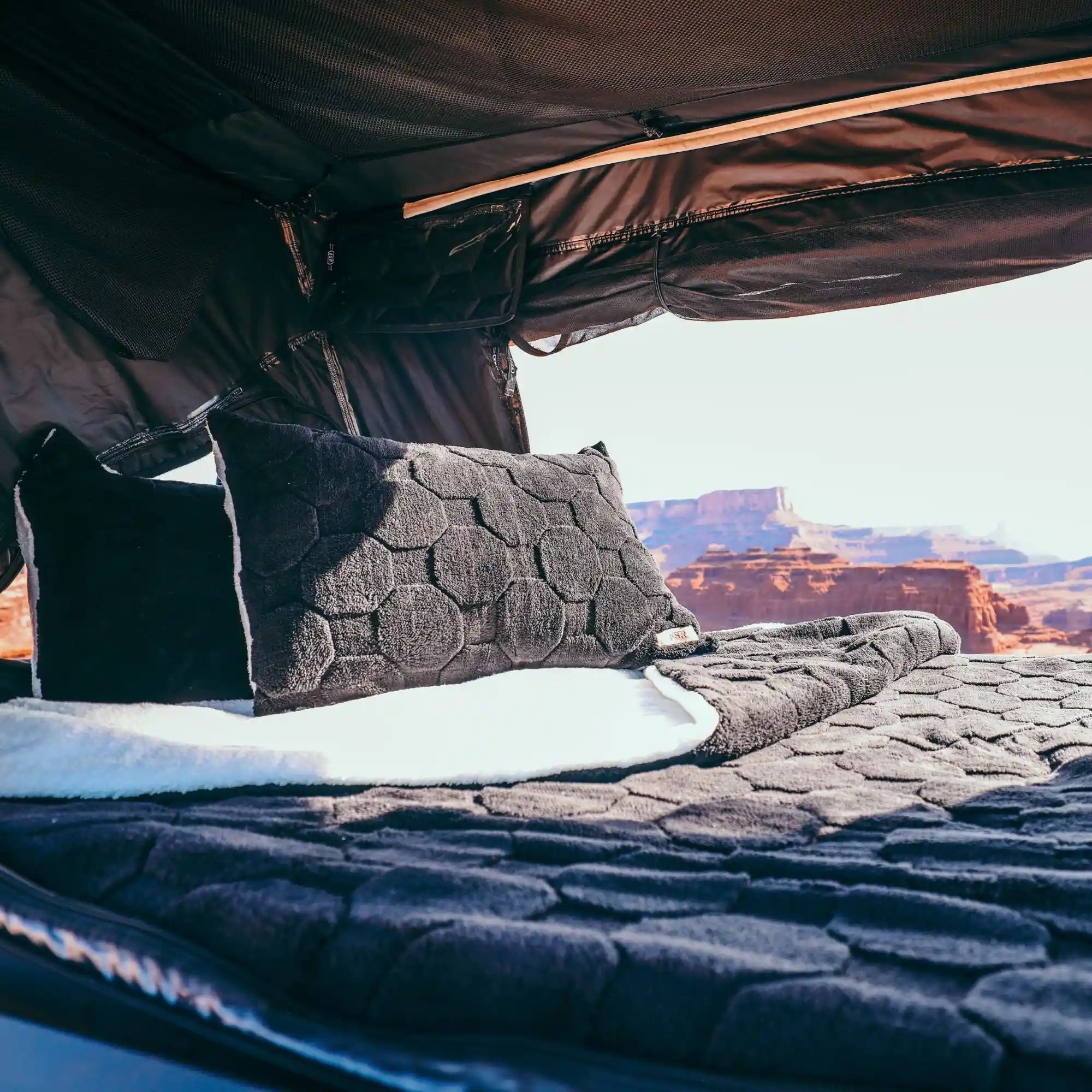 View looking out of an FSR rooftop tent with sleeping area inside made with pillows and blankets from Freespirit Recreation in the foreground and a scenic desert landscape in teh background.