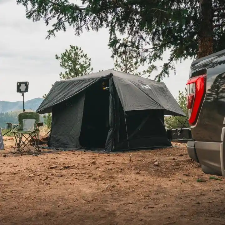 Camping setup with a Freespirit Recreation Hub pop-up camping tent, camp chair, and vehicle parked in a forested area with mountains visible in the background