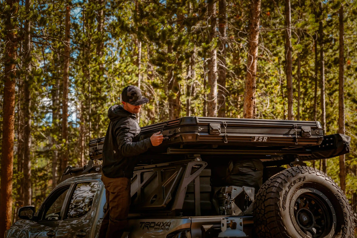 Person opening an FSR Rooftop Tent equipped with tent accessories from Free Spirit Recreation in a forested campsite setting