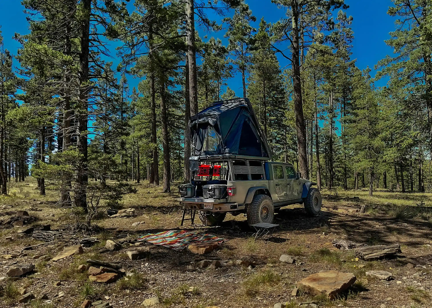FSR Jeep Gladiator tent setup in a wooded campsite beneath a blue sky 