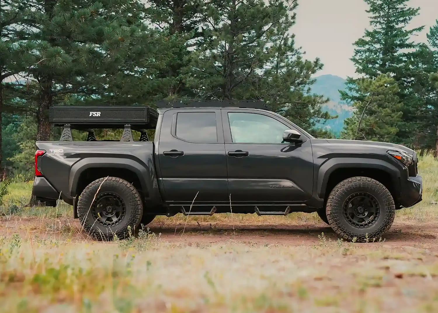 Short Bed Toyota Tacoma pickup with an FSR rooftop tent from Free Spirit Recreation mounted below the cab and parked in a wooded campsite 