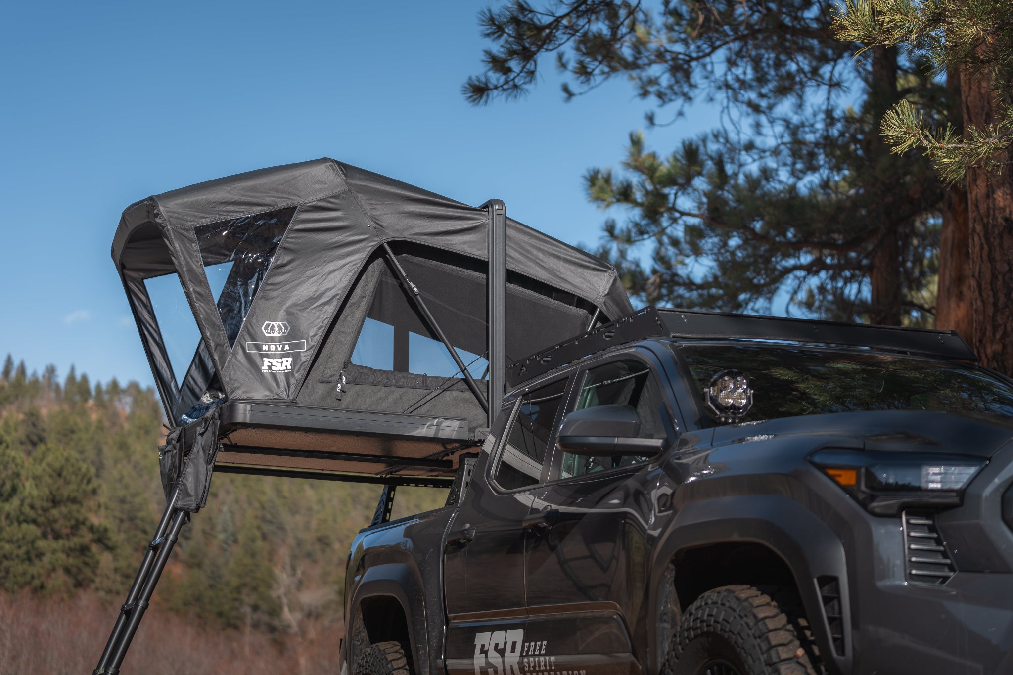 Black Toyota Tacoma truck with a Nova rooftop tent in a forest setting