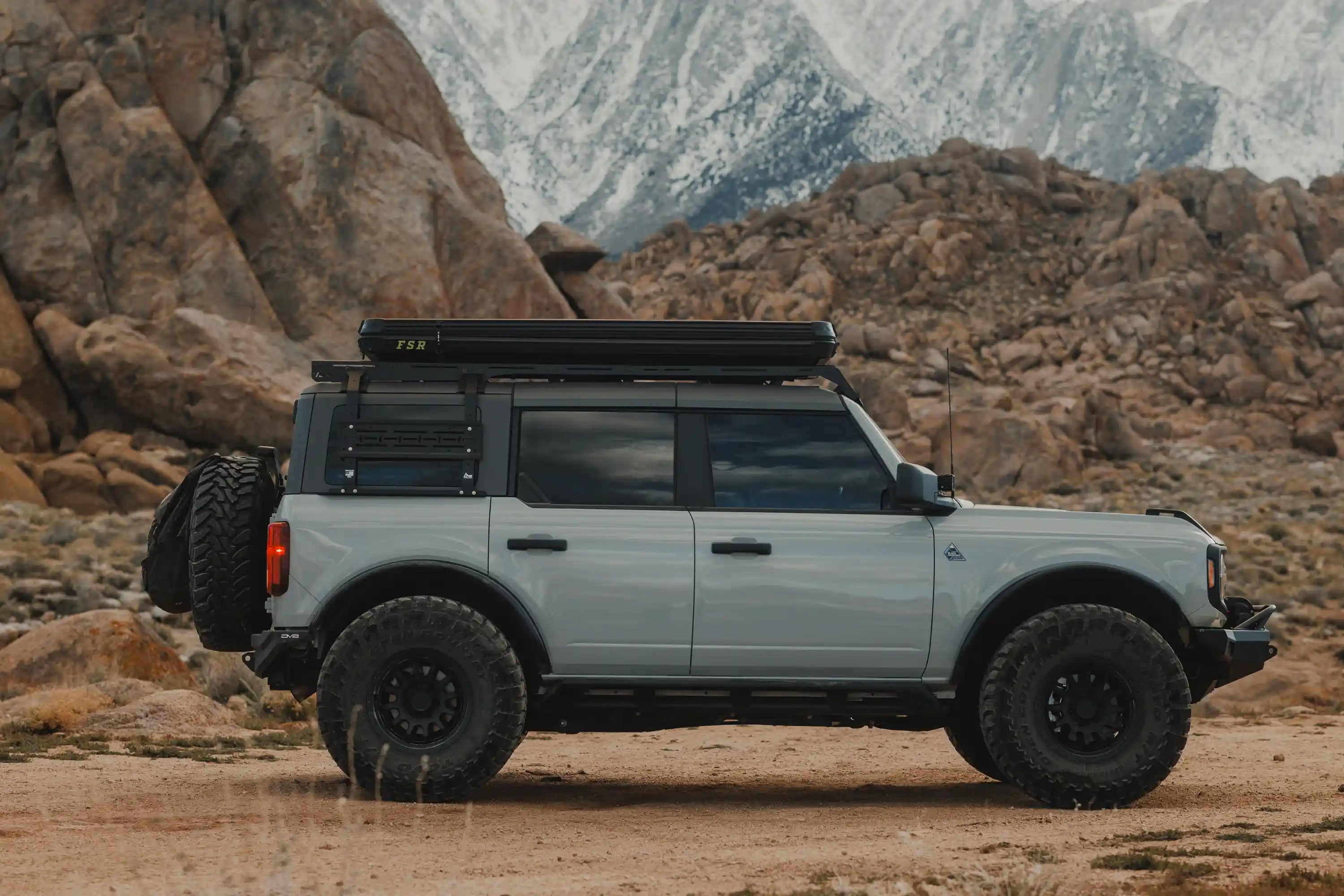 Ford Bronco with an FSR Rooftop Tent mounted to the roof rack, parked in a desert campsite with snow covered mountains in the background