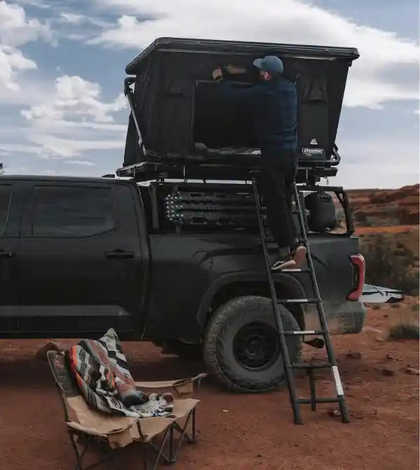 Person wetting up an FSR rooftop tent mounted to a truck bed rack while camping in a desert setting