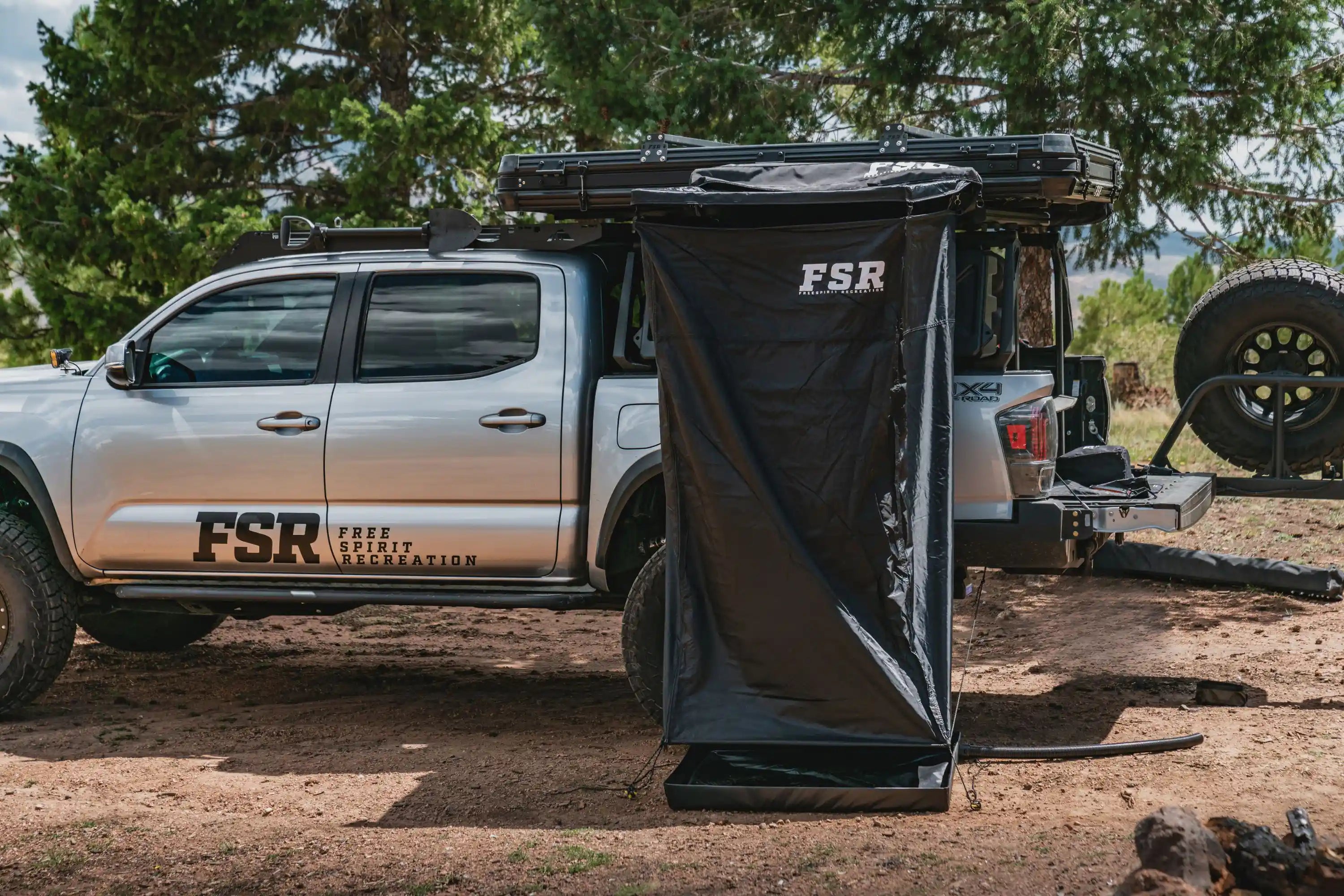 Person using the FSR Shower Awning while truck camping in a wooded campsite.