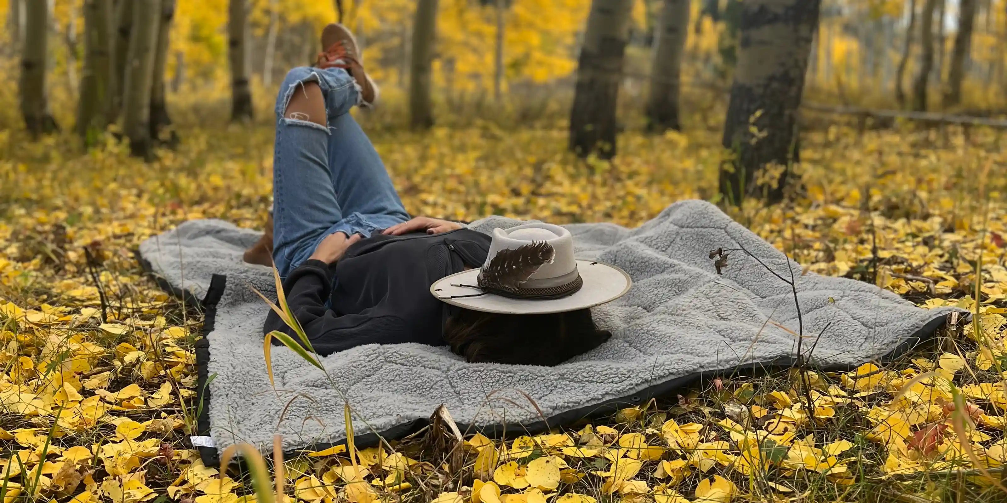 Person sleeping on FSR camping bedding in a forest surrounded by yellow fall leaves using Free Spirit Recreation camping sleeping gear.