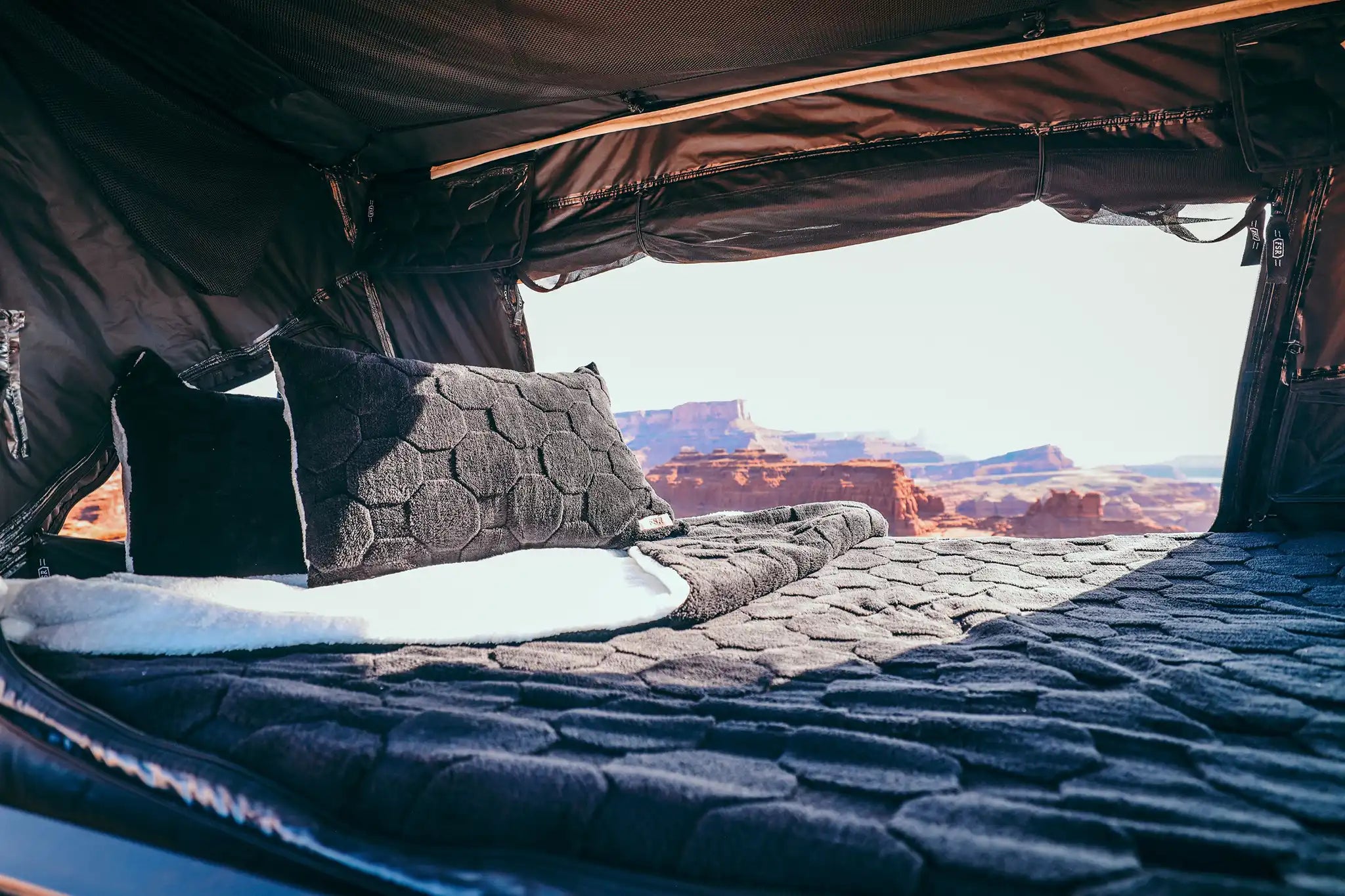 Interior of an FSR Rooftop Tent with Cloud Comforter and pillow cases setup with a scenic desert landscape visible behind the bedding set