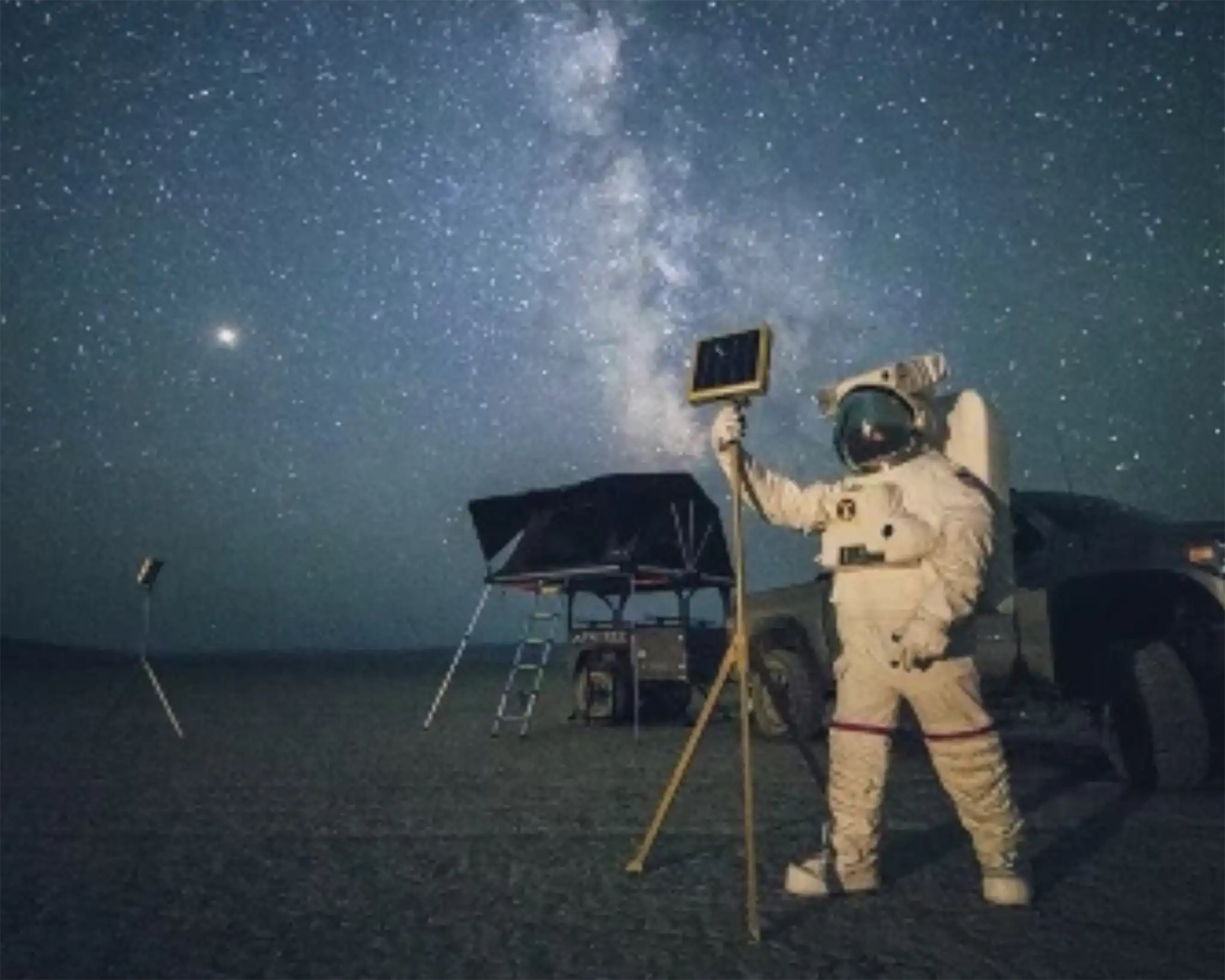 2019 FSR promo image with a Person in a spacesuit holding an FSR ReadyLight LED camp light with an overland trailer equipped with a Free Spirit Recreation Rooftop Tent in the background under a starry sky