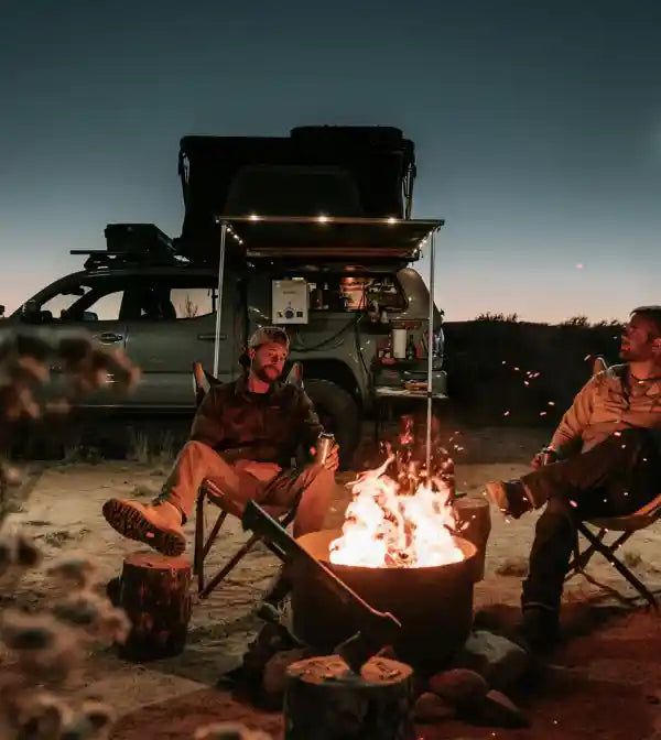 Two people sitting by a campfire in the desert at night with a vehicle in the background equipped with an FSR Rooftop Tent and Awning