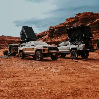 Two trucks equipped with Freespirit Recreation rooftop tents and an FSR Hub pop-up tent setup for camping in a desert landscape surrounded by red rock