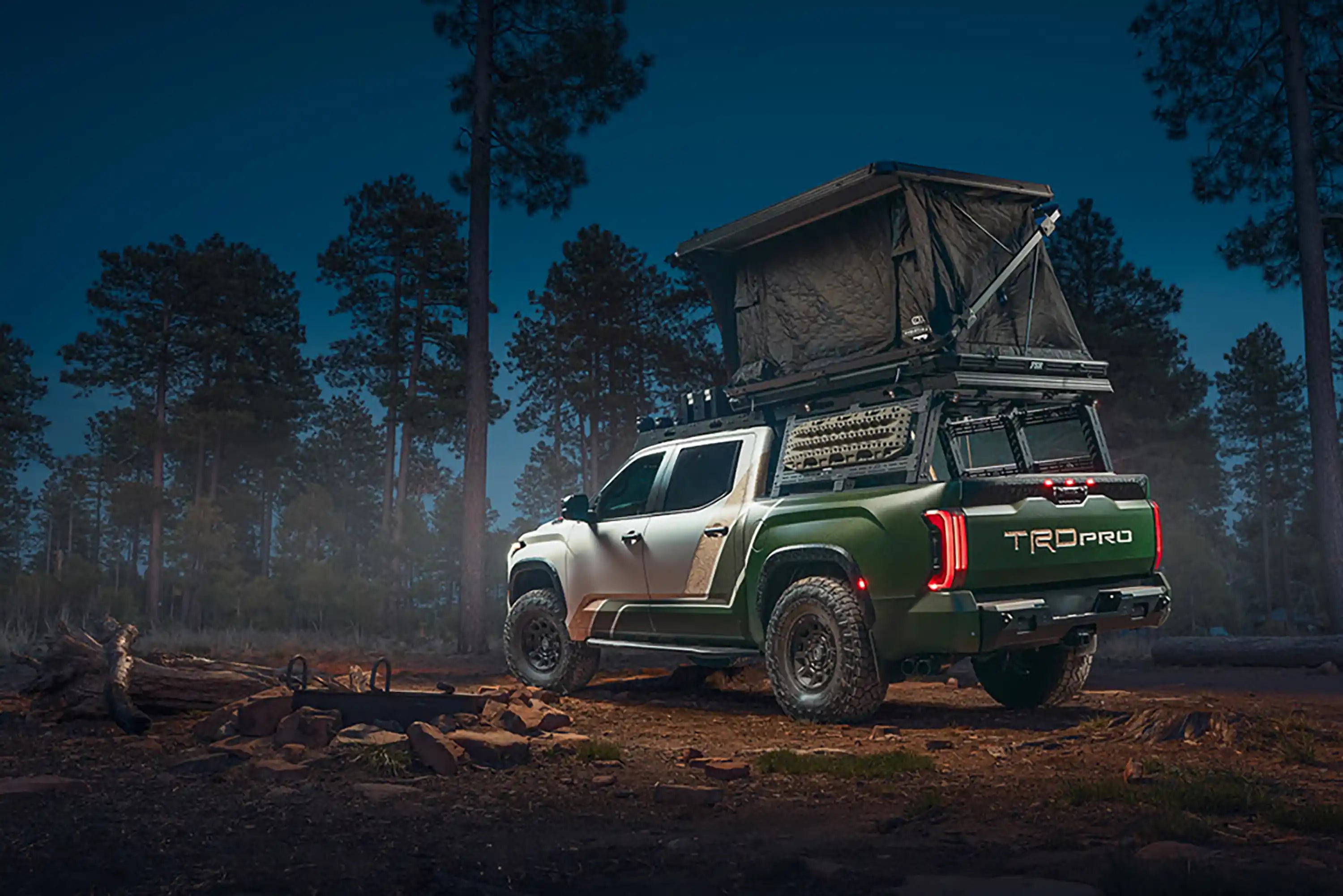 Toyota Tundra with FSR Rooftop Tent by Freespirit Recreation installed on the truck's bed rack and setup for camping at a forested campsite at night