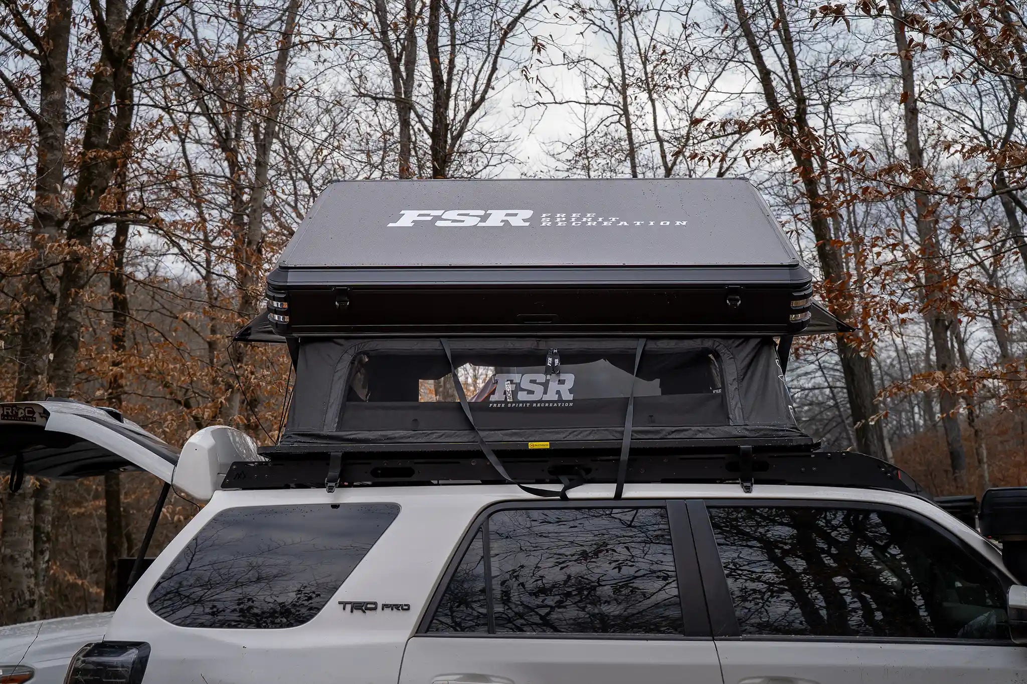 Rear-facing image of the FSR Kali King Rooftop Tent setup while camping in a wooded area with windows open