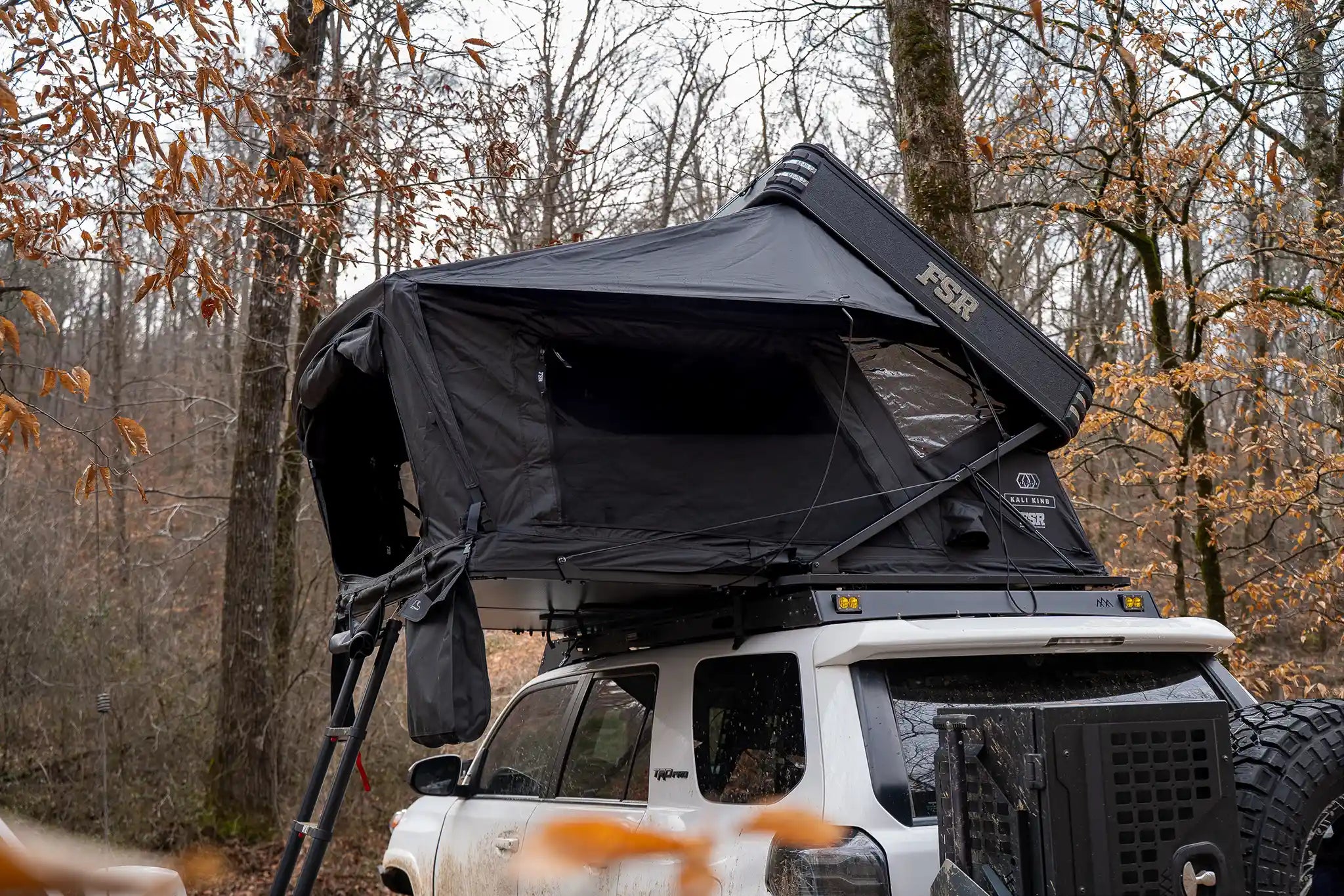 FSR Kali King Rooftop Tent mounted on a white Toyota 4Runner, open and setup for camping in a heavily wooded campsite 