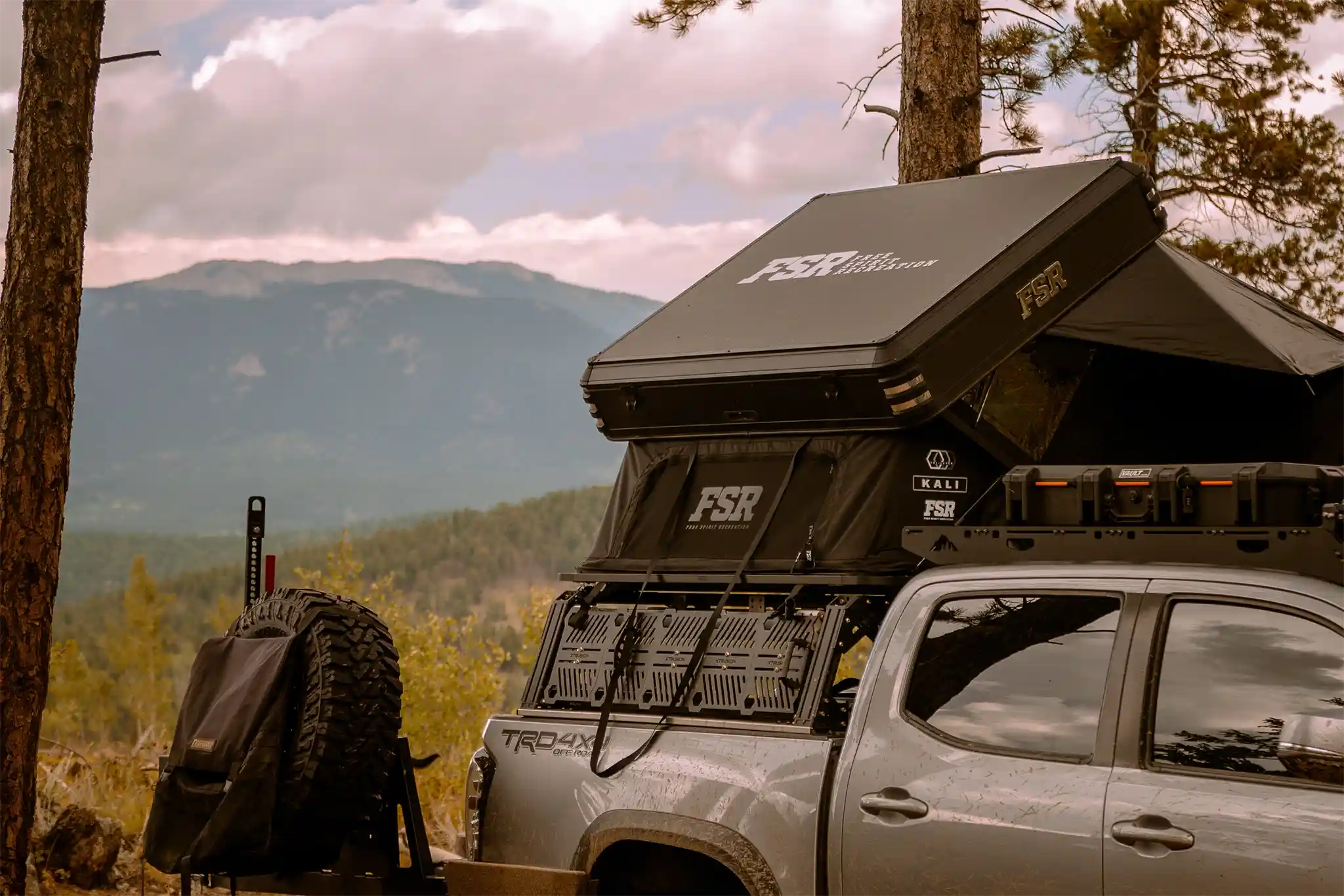 FSR Kali rooftop tent from Free Spirit Recreation mounted and setup on an off road truck in a forested area with mountains in the background
