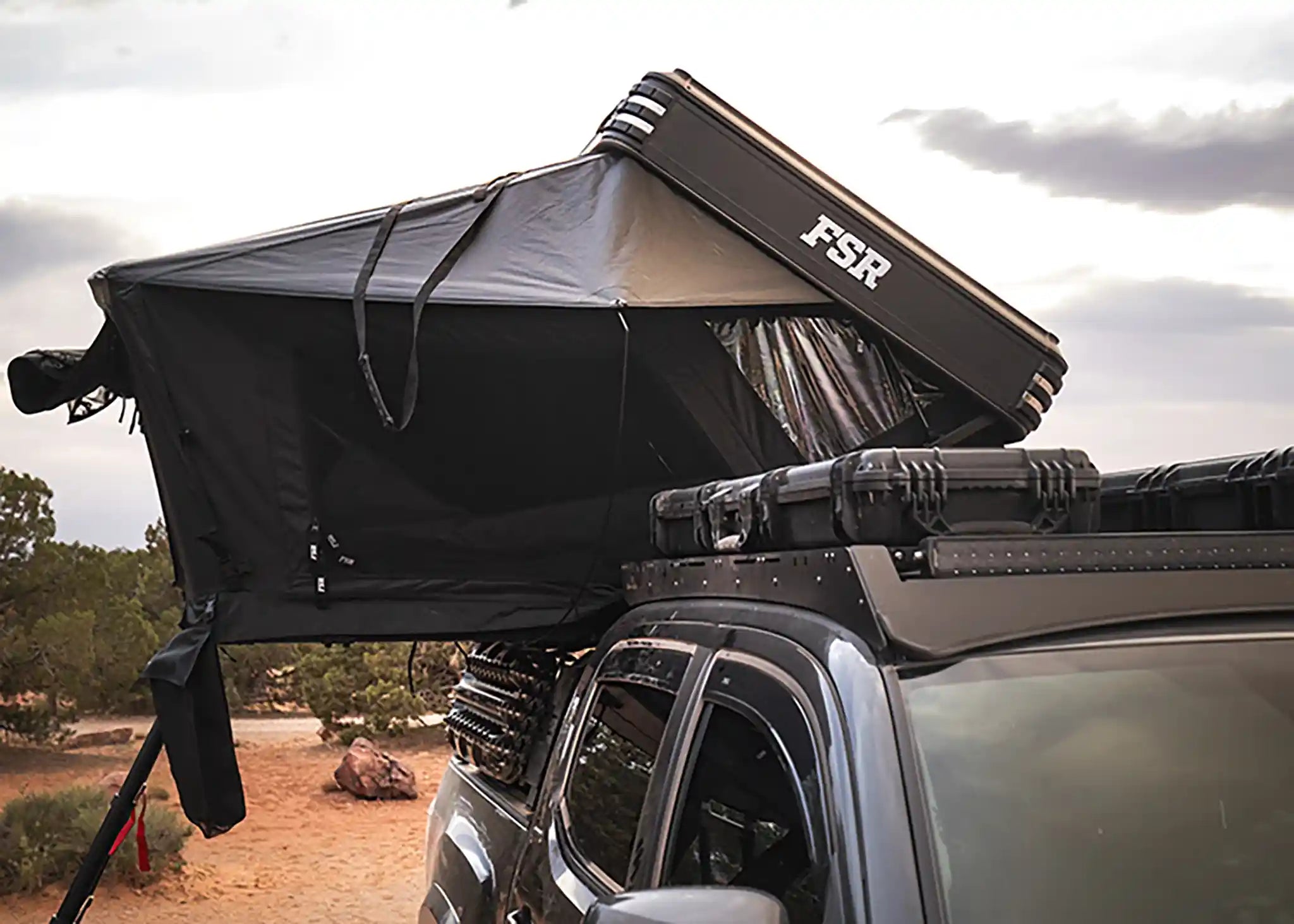 FSR Kali rooftop tent from Free Spirit Recreation setup on a truck rack with ladder and shoe bag accessories in use against a desert campsite background