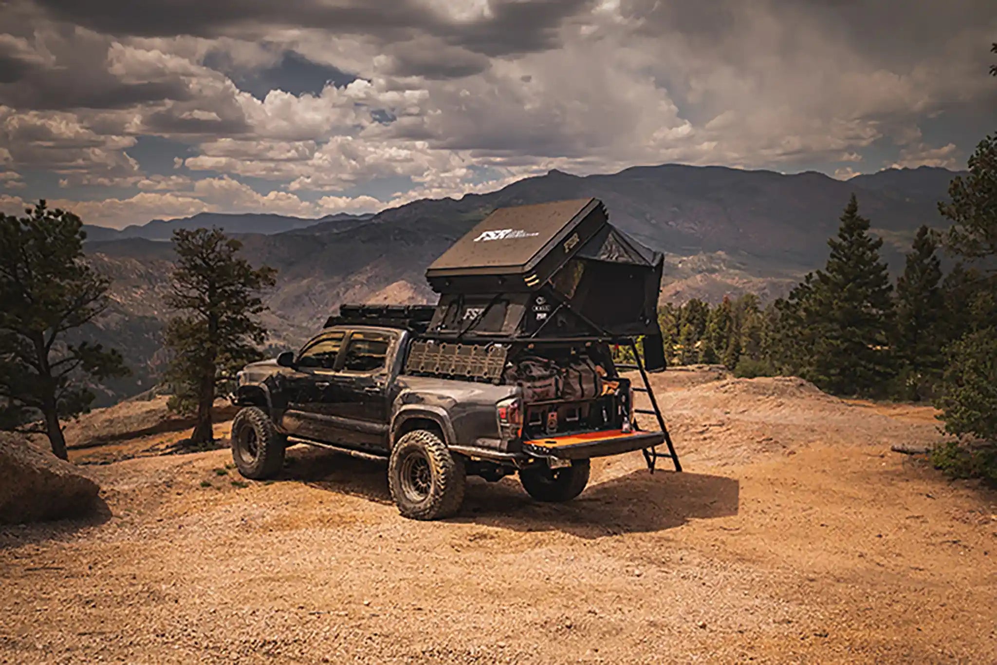 Black overland Toyota Tacoma build  with an FSR Kali rooftop tent setup on the bed rack parked on a dirt campsite with mountains in the background