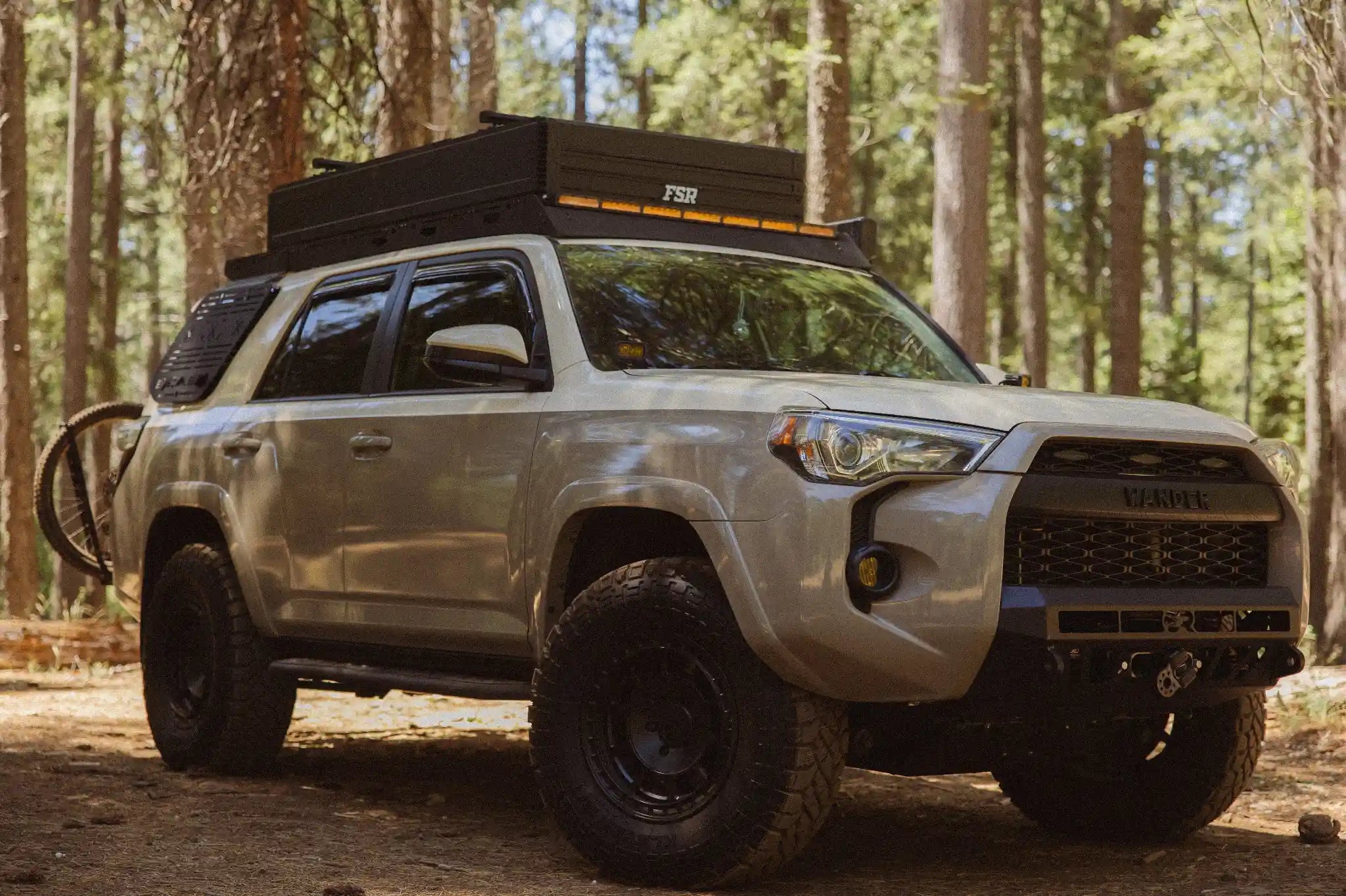 Silver Toyota 4Runner with roof rack and bike on a dirt road in a forest with FSR Nova King Rooftop tent from Free Spirit Recreation on top.