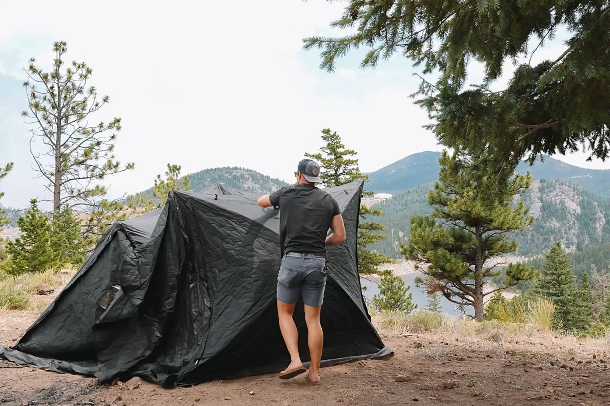 Person setting up an FSR Hub pop-up camping tent using instruction manual from Free Spirit Recreation in a scenic campsite with mountains and a body of water in the background