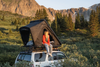 Person sitting inside an FSR rooftop tent on a vehicle with mountains and trees in the background