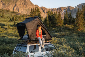 Person sitting inside an FSR Aspen Pro roof top tent installed on a 3rd Gen 4Runner in an alpine campsite with mountains and trees in the background