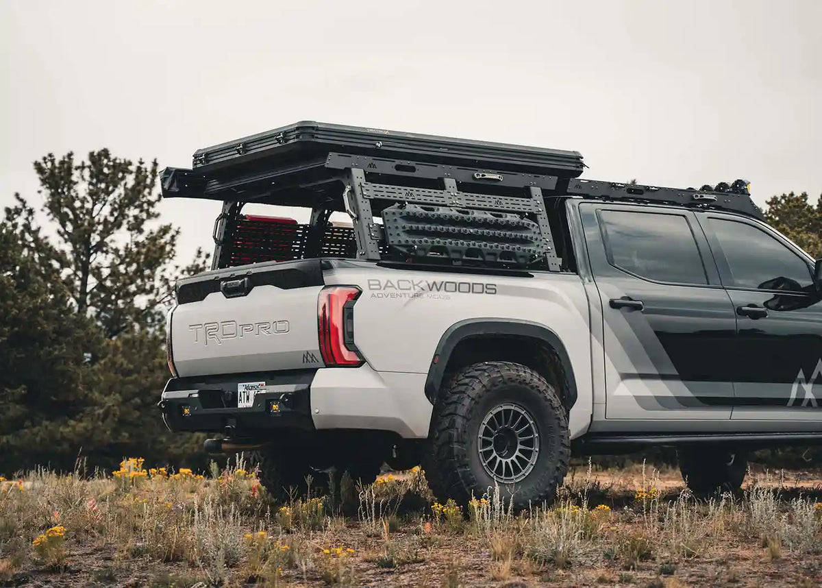 Tundra driving off road with roof top tent, awning, auxillary fuel tanks, and traction boards mounted to the Backwoods Adventure Mods Full Height Toyota Tundra Bed Rack | Free Spirit Recreation